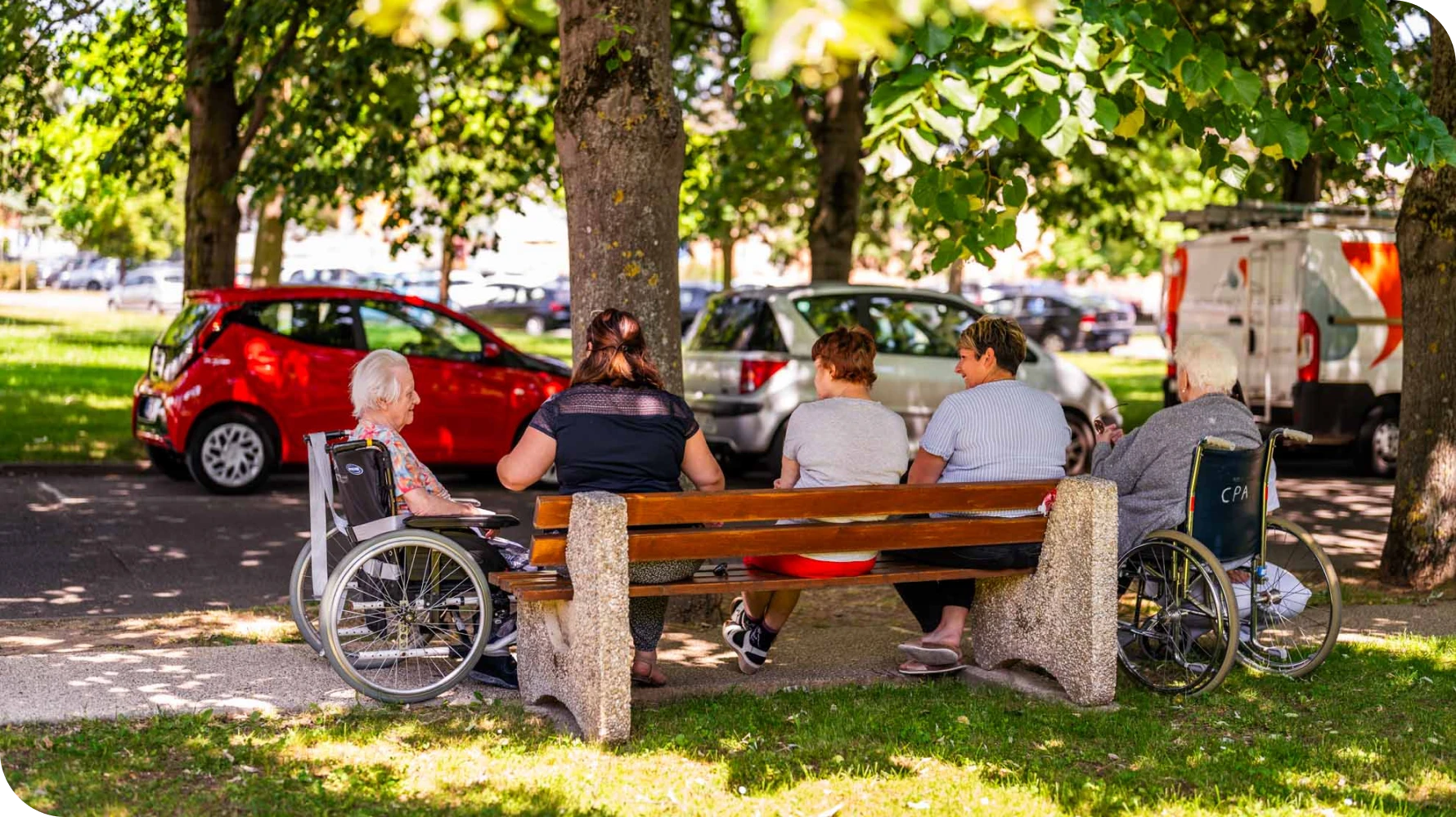 Résidents et accompagnants en extérieur, fauteuil roulant sous les arbres
