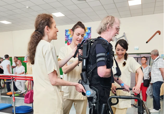 Patiente équipée d’un exosquelette de rééducation, accompagnée par deux soignantes